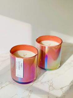 two candles sitting next to each other on top of a white counter with a label