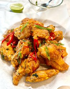 chicken wings with red peppers and green onions on a white paper towel next to a glass bowl