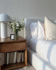 a bed with white sheets and pillows next to a wooden night stand filled with books