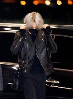 a woman walking down the street with her hand on her head, wearing a black leather jacket