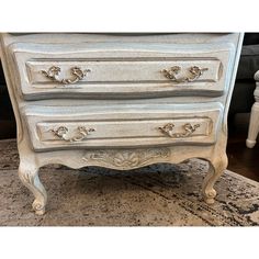 an antique white dresser with gold trimmings on it's legs and drawers