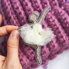 a hand holding a small white ballerina brooch on top of a purple crocheted bag