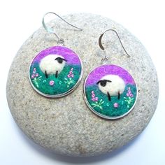 a pair of earrings with a sheep on it sitting on top of a rock next to a stone