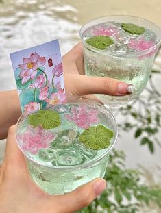 two people holding up glasses filled with water and flowers