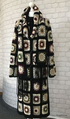 a black and white crocheted coat hanging on a wall next to a brick wall