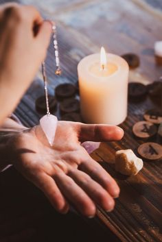 a person's hand on a table next to some rocks and a candle