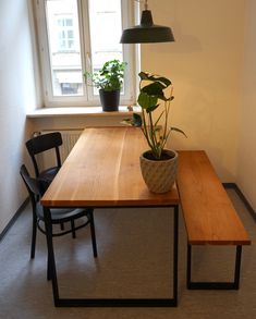 a wooden table with two chairs and a potted plant on it in front of a window