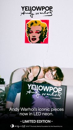 two women laying on top of a bed next to a yellowpop sign with the words, andy warhol's iconic pieces now in led neon