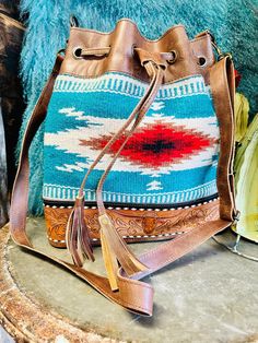 Grissom Steer Tooled Leather Bucket Bag Artisan Bucket Bags For Travel, Artisan Bucket Travel Bag, Artisan Bucket Bag With Adjustable Strap, Multicolor Bucket Bag With Dust Bag, Artisan Turquoise Bag For Everyday Use, Artisan Turquoise Bags For Everyday, Hand Tooled Leather Bags For Rodeo, Leather Fringe Bucket Bag For Daily Use, Artisan Turquoise Shoulder Bag For Everyday