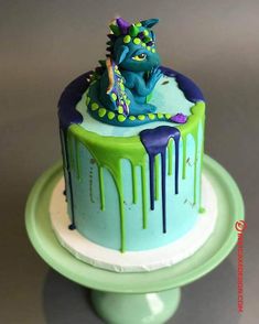 a blue and green birthday cake with a dragon on it's icing drips