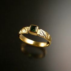 a close up of a gold ring with a green stone in it on a black surface