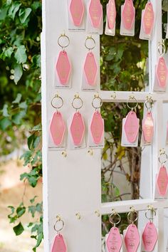 pink and gold keychains hanging from a white wall with tags attached to them