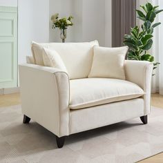 a white couch sitting on top of a wooden floor next to a potted plant