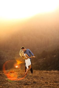 a man and woman kissing in front of the sun on top of a hill at sunset