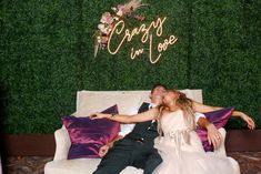 a bride and groom laying on a couch in front of a green wall that says crazy i'm yours