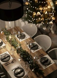 the table is set for christmas dinner with silverware and greenery on wooden planks