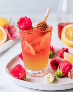 there is a drink with lemon and honey on the table next to some red flowers