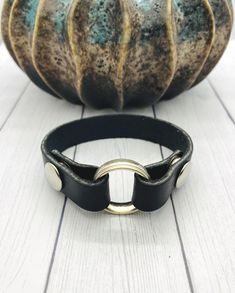 a black leather bracelet with two gold rings on it next to a ceramic pumpkin ornament