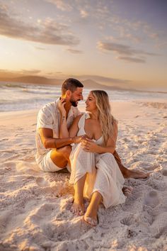 a man and woman sitting on the beach at sunset