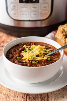 a white bowl filled with chili and cheese on top of a plate next to an instant pot