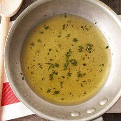 a silver bowl filled with soup on top of a wooden table next to a spoon