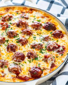 a cheesy pizza with meatballs and cheese in a pan on a checkered table cloth