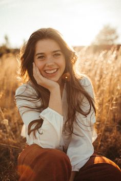 a woman sitting in the middle of a field smiling