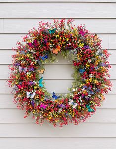 a colorful wreath hanging on the side of a white house with butterflies and flowers all over it