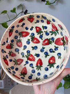 a hand holding a bowl with strawberries and blueberries painted on the outside in red white and blue