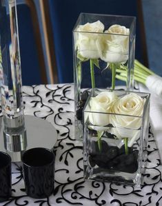 three vases filled with white roses sitting on top of a black and white table cloth