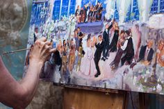 a woman is painting on an easel in front of a wall with many people