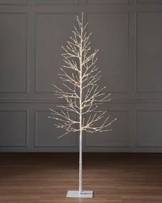 a white christmas tree with lights on it in front of a gray wall and wooden floor