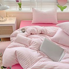 a laptop computer sitting on top of a bed covered in pink and white striped sheets