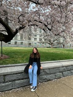 a woman sitting on a stone wall next to a tree with pink flowers in bloom