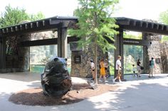 people are walking around in front of the entrance to a park with rocks and trees