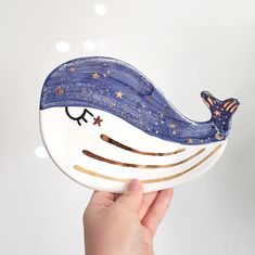 a hand holding a white and blue plate with a whale design on it's face