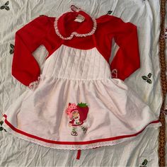 a red and white dress with strawberrys on the bottom is laying on a bed