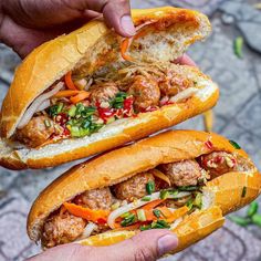 two sandwiches with meat, vegetables and sauce being held up by someone's hands