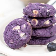 three cookies with white chocolate chips and blueberries on a plate next to some blackberries