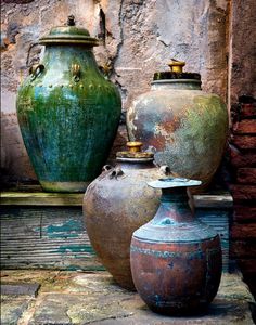 three large vases sitting on top of a wooden table next to a brick wall