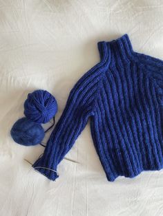 a blue sweater and ball of yarn on a white sheet