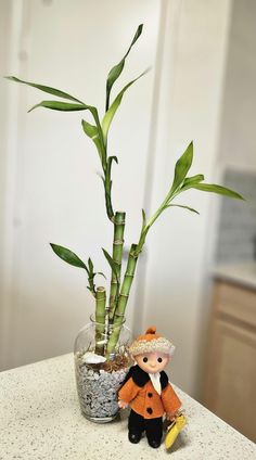 a small doll next to a potted bamboo plant on a counter in a kitchen