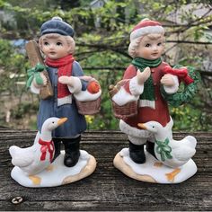 two figurines are sitting on a wooden table outside with trees in the background