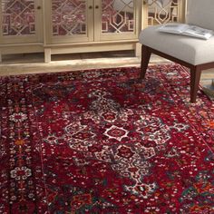 a red rug with an ornate design on the floor and sideboard in the background