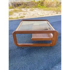 a wooden table with glass top sitting on the ground in front of some grass and bushes