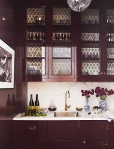 a kitchen with wooden cabinets and marble counter tops, wine glasses on the cabinet doors