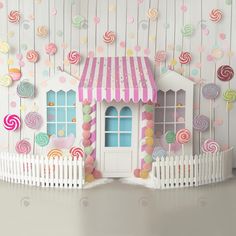 a paper house with candy and lollipops hanging from the ceiling next to a white picket fence