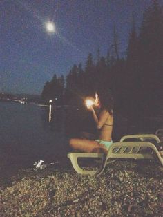 a woman sitting on top of a beach next to the ocean at night with a flashlight in her hand