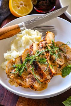 a white plate topped with chicken and mashed potatoes next to a knife and fork