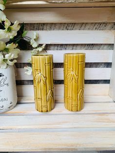 two yellow vases sitting next to each other on a wooden bench with flowers in the background